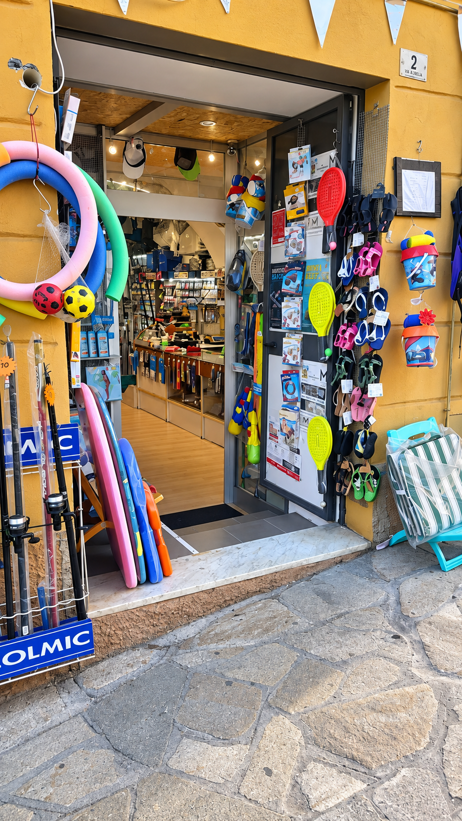 L'ingresso del negozio in Via del Collegio 2 a Imperia: accanto alla porta, canne da pesca ed articoli da mare come ciambelle, racchettoni, infradito e secchielli